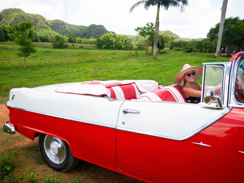 Victoria sitting in the driver's seat of a red and white vintage car in Cuba