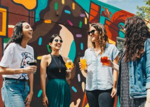 Group of friends in front of a colorful mural holding drinks